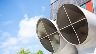 Industrieller Hintergrund von zwei großen modernen Belüftungsrohroberteilen vor blauem Himmel (verweist auf: Neues Energielabel für komplexe Klima- und Lüftungsanlagen in Nichtwohngebäuden)