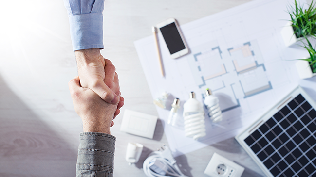 verweist auf: Anbieterliste Architektenplan, Glühbirnen, Smartphone und Solarzellen auf einem Tisch, obendarüber geben sich 2 Menschen die Hände (verweist auf: Anbieterliste)